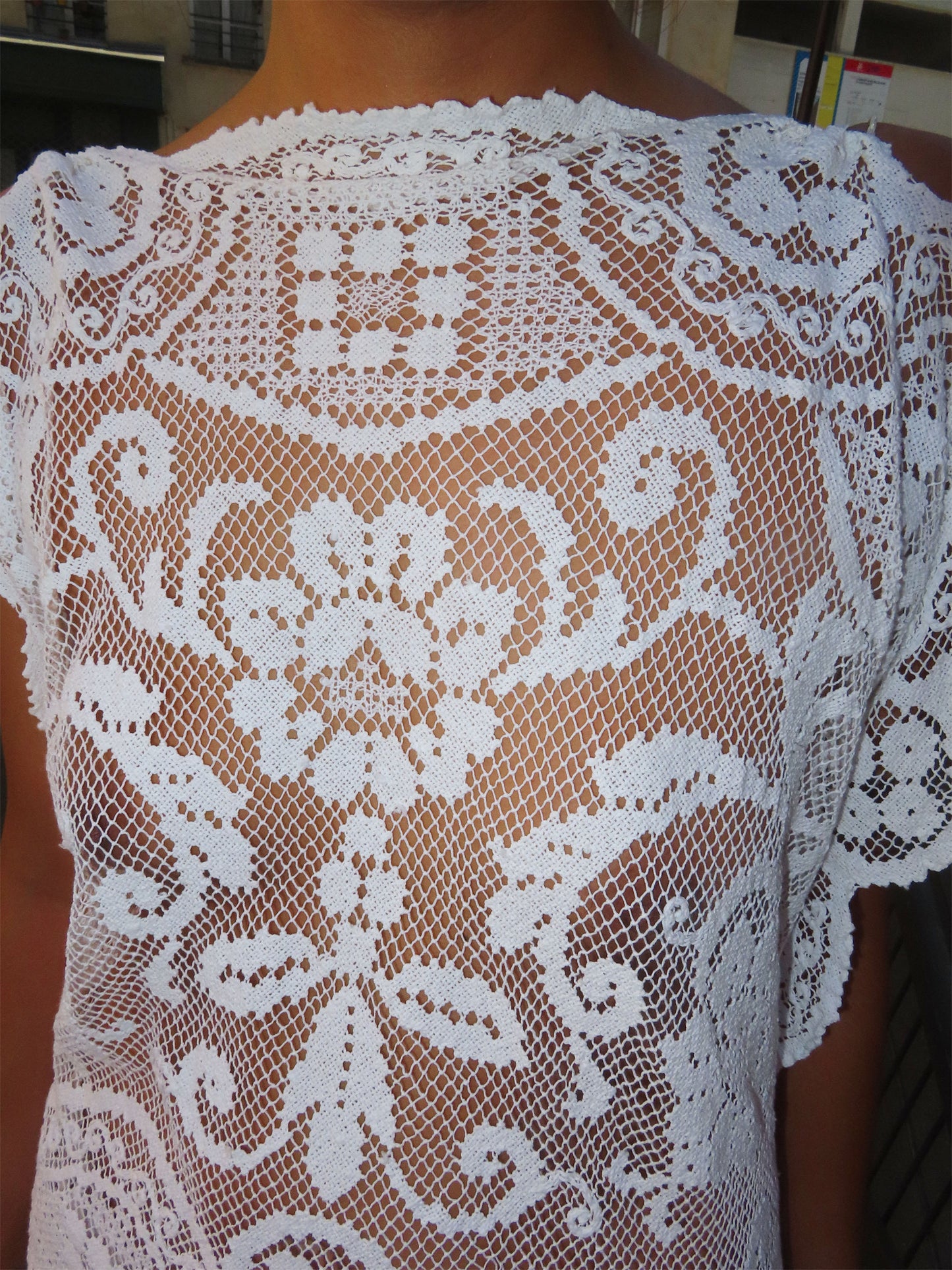White lace top with intricate floral and scroll patterns, shown on a model from the back.